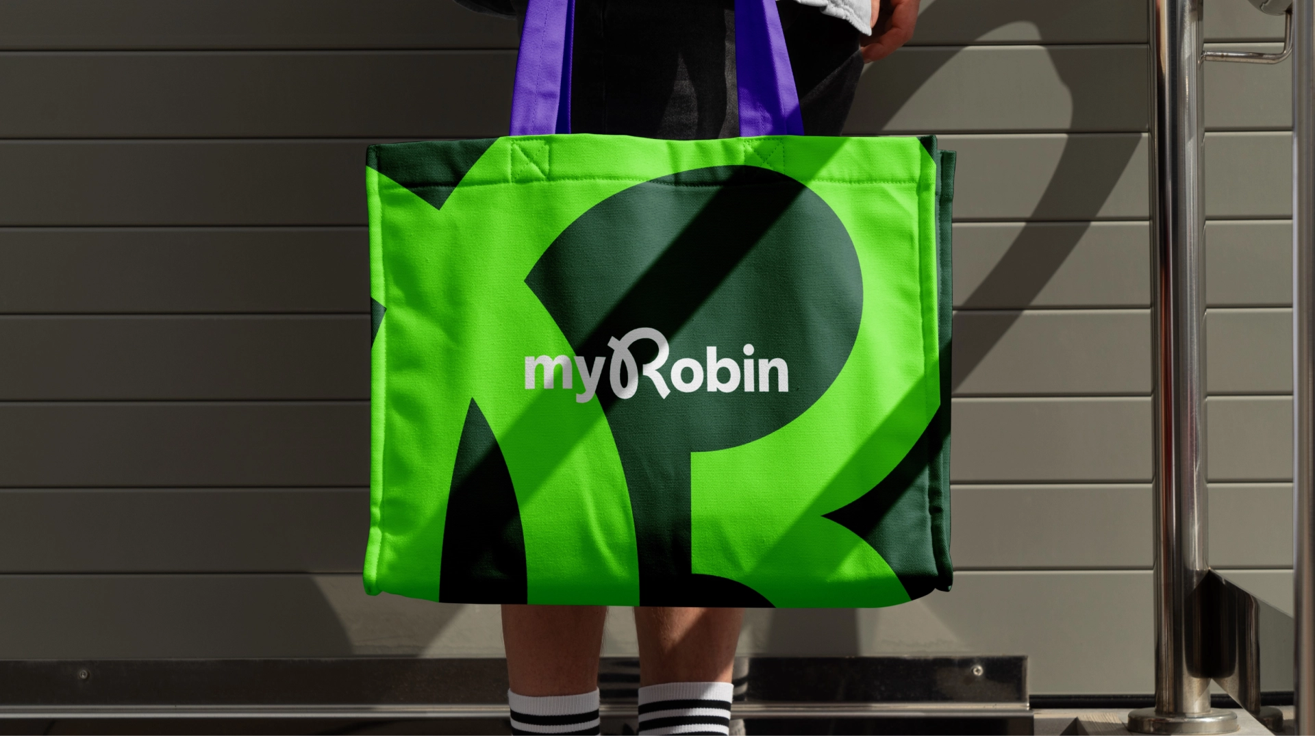 Person hält eine große Stofftasche mit dem myRobin Brand Logo. Die Tasche ist mit den auffälligen Grüntönen der Brand Colors gestaltet.